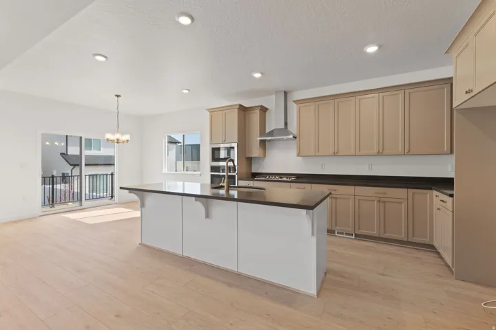 Kitchen featuring wood-finish flooring, recessed lighting, central island with dark countertop, built-in stainless steel appliances, and a sliding glass door to an exterior balcony