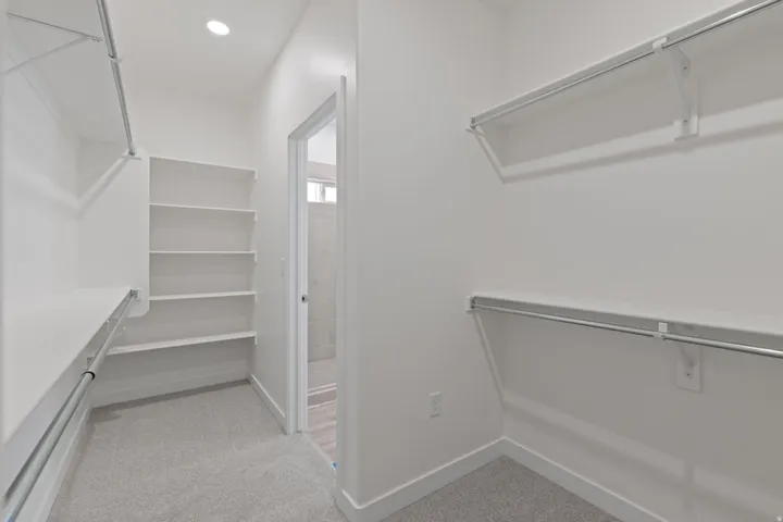 Recessed ceiling lighting, soft gray carpet, white built-in shelving, and hanging rods