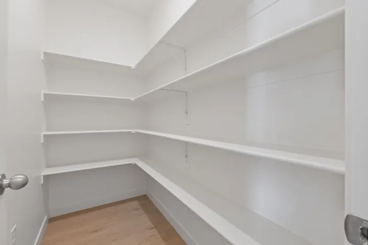 Expansive pantry featuring multi-level shelving, bright white walls, and wood-finish flooring