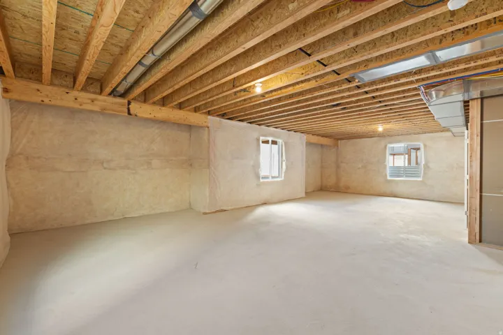 Unfinished basement with exposed wood joists, concrete flooring, two windows, and insulated walls