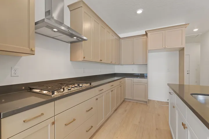 Kitchen featuring light-toned cabinetry, stainless steel range hood, built-in gas cooktop, dark countertops, and wood-finish flooring