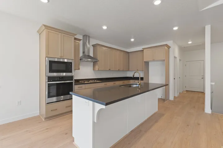 Modern kitchen featuring light wood-finish flooring, recessed lighting, stainless steel appliances, a kitchen island with a dark countertop, and light-toned cabinetry