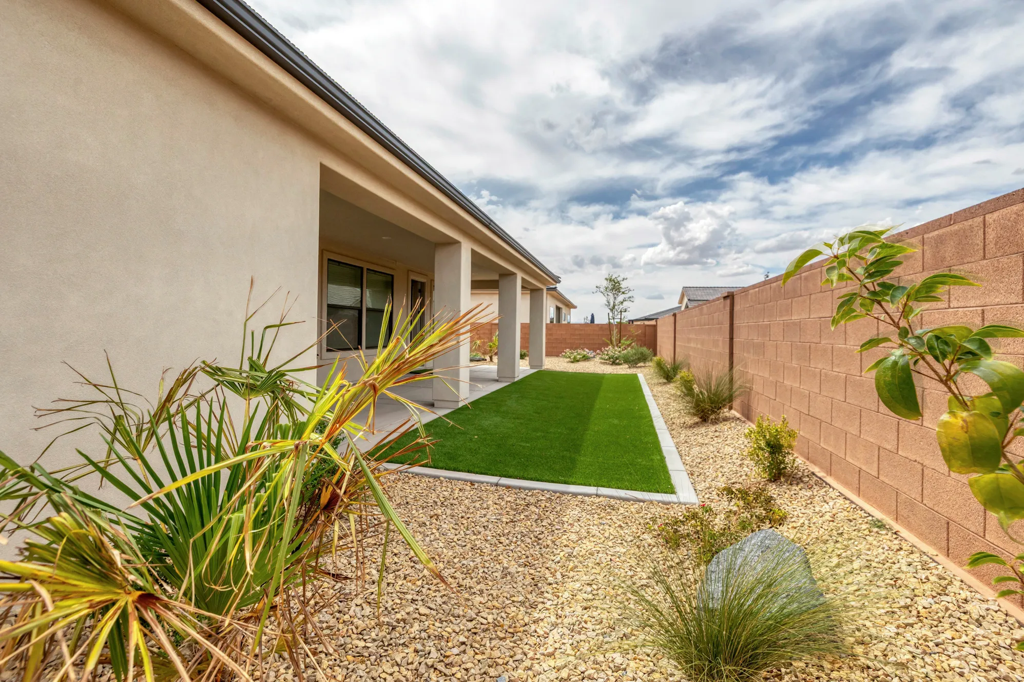 Private backyard featuring a covered patio, artificial turf, gravel landscaping, and block walls