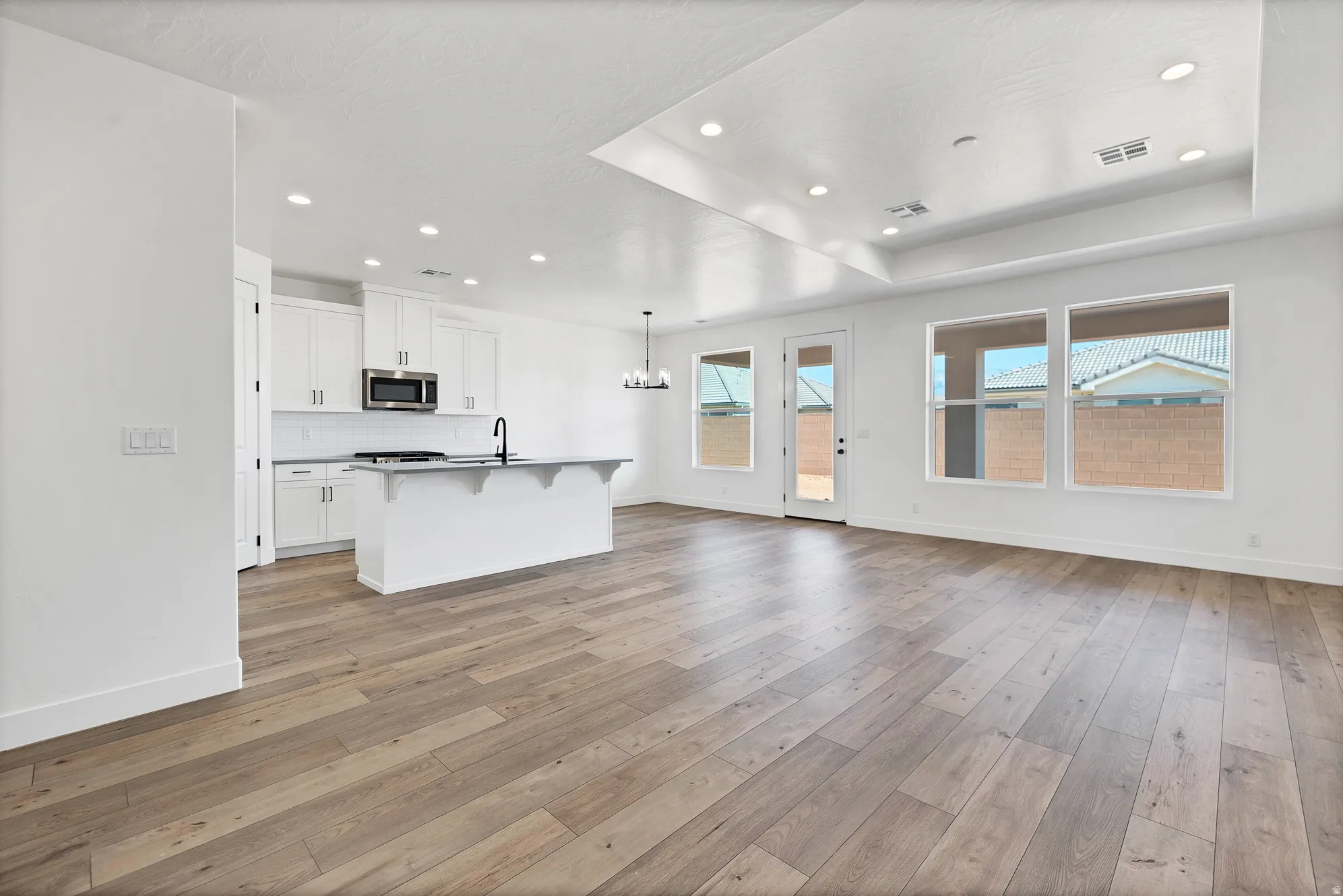 Open-concept living space with wood-finish flooring, recessed lighting, and a tray ceiling