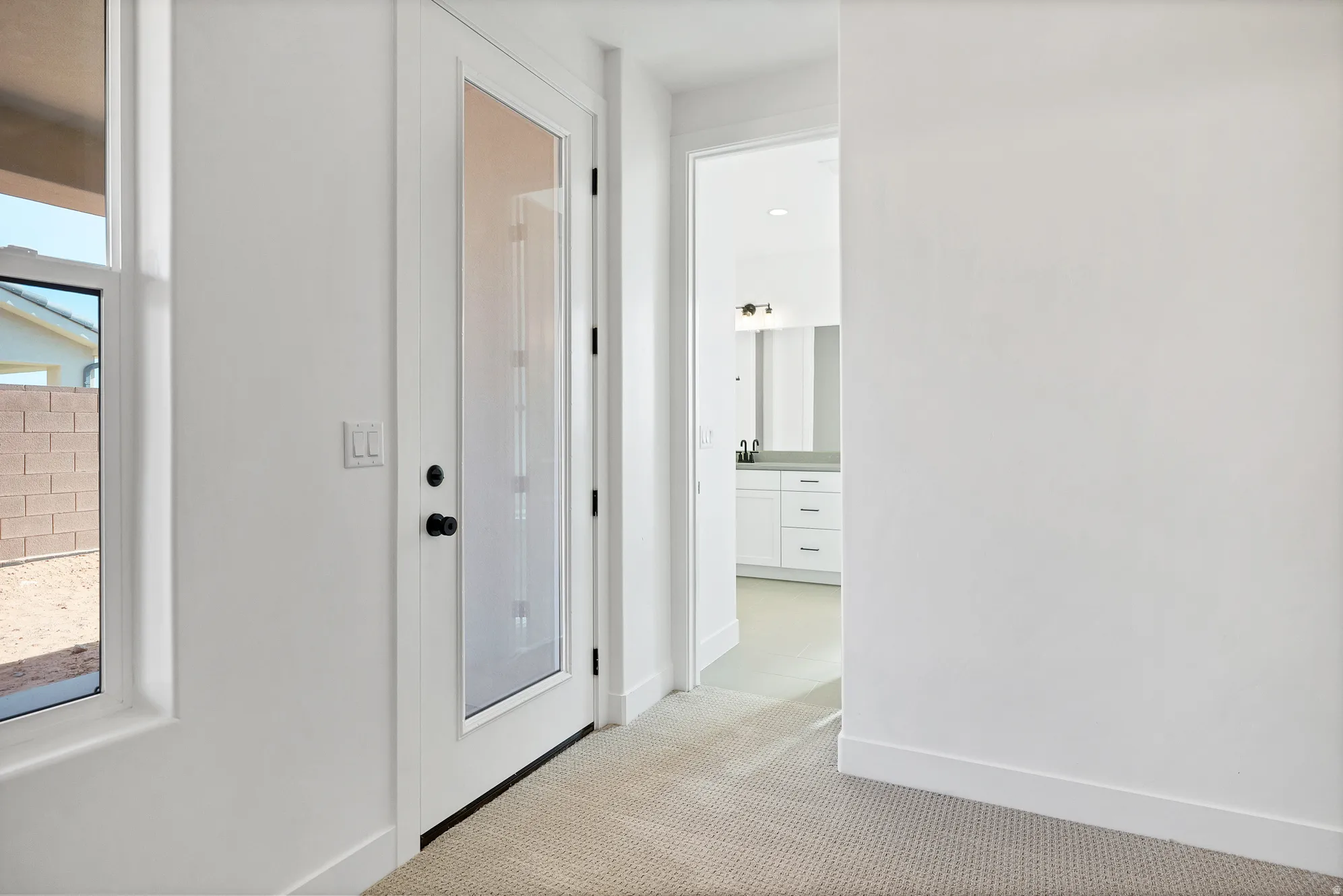 Frosted glass entry door with matte black hardware, bright white walls, and neutral carpet flooring