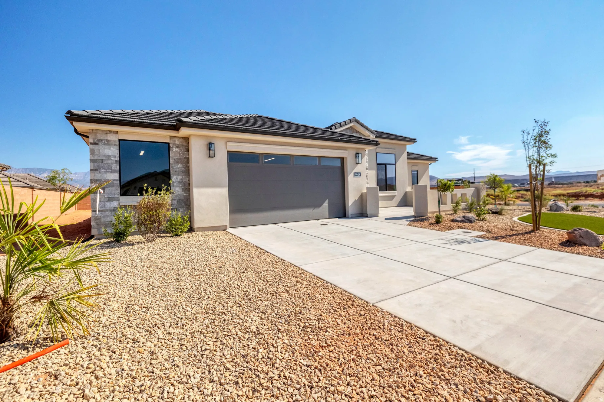 Contemporary stucco exterior with stone accents, a dark-tiled roof, and an integrated garage