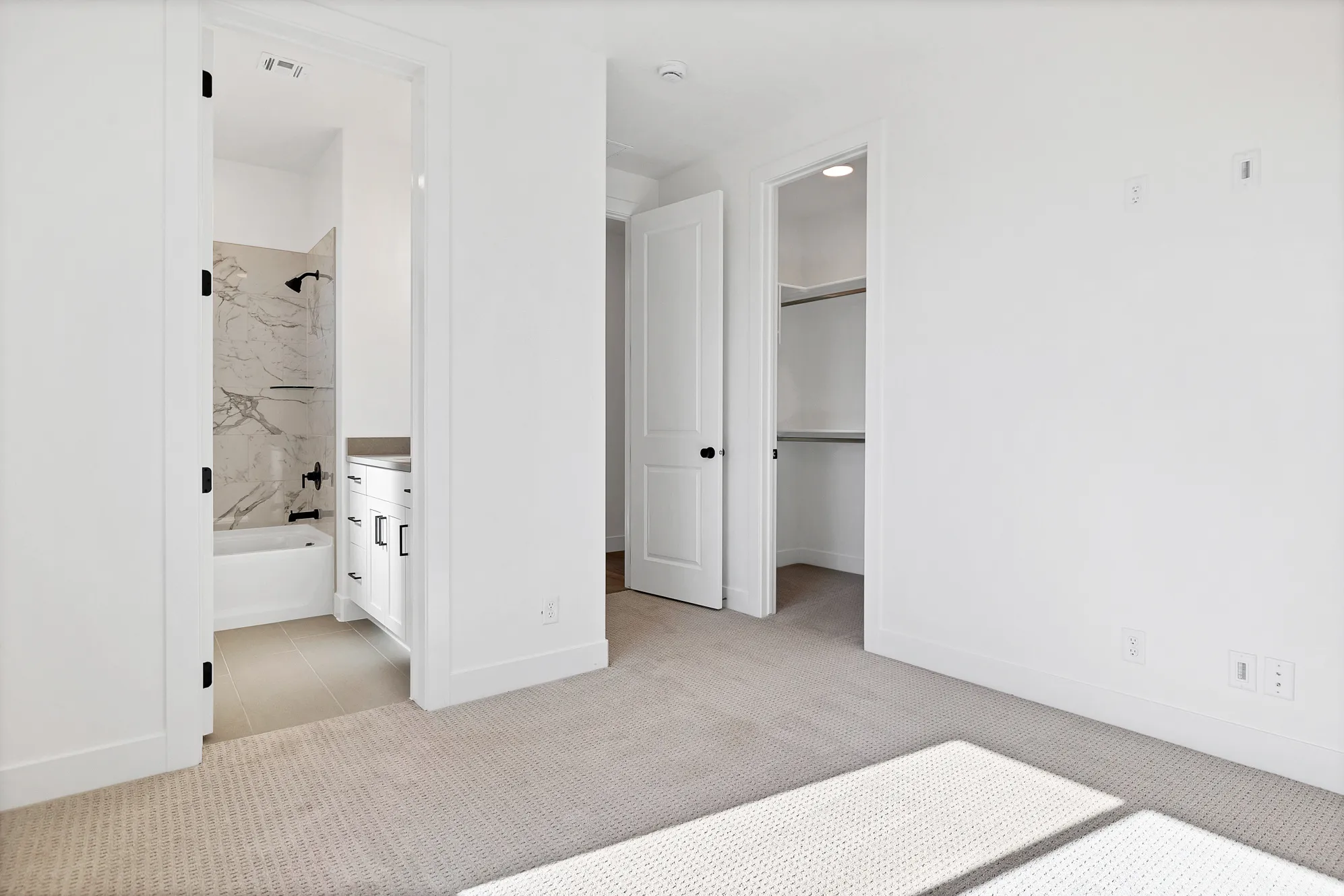 Light-colored carpeted flooring, white walls, and a white interior door with black hardware