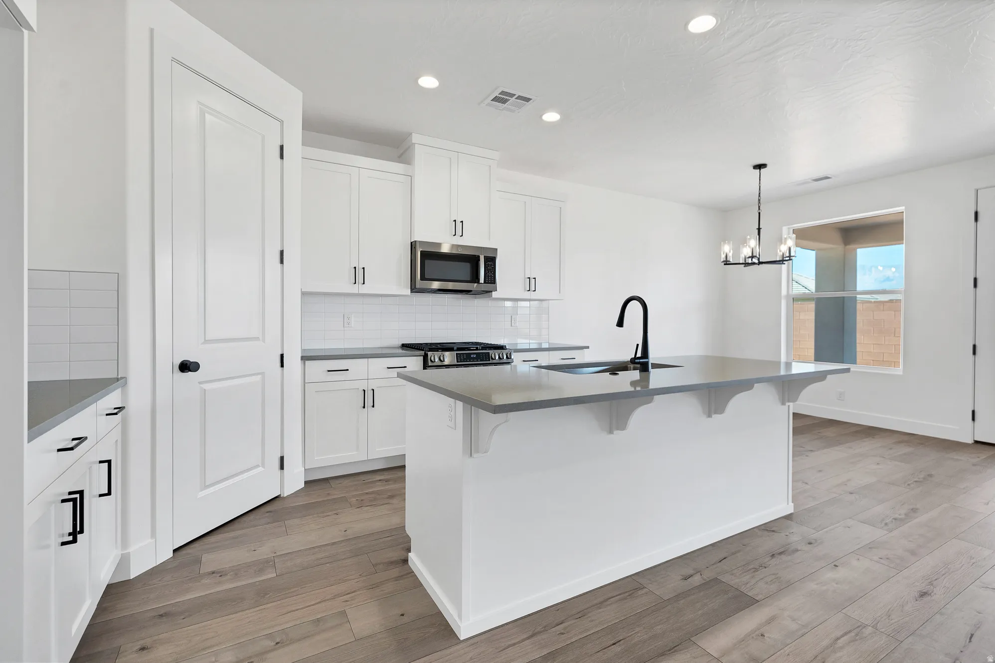 Kitchen featuring white cabinetry, stainless steel appliances, a center island with sink, and wood-finish flooring