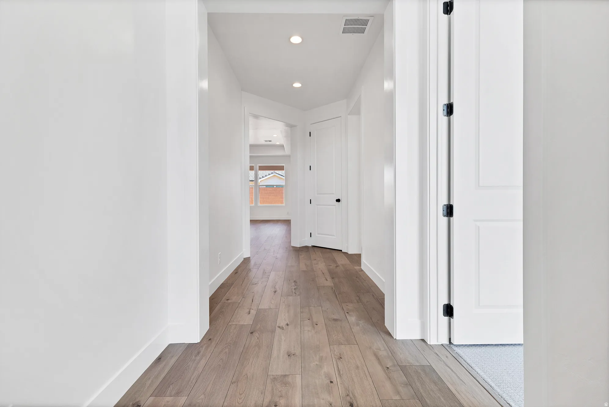Hallway featuring wood-finish flooring, recessed lighting, white panel doors, and a bright interior