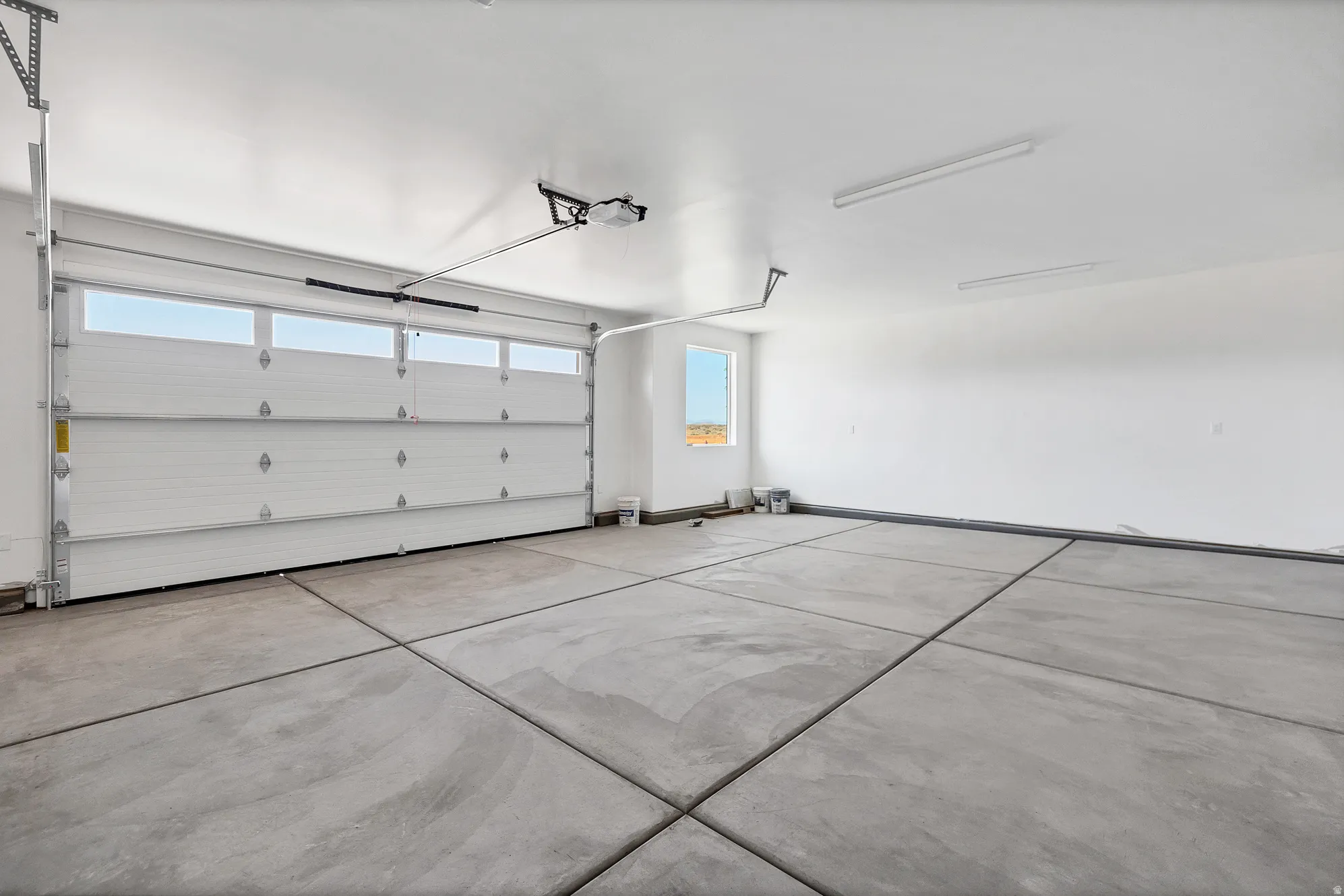 Attached garage with a white sectional door featuring upper transom windows, an automatic opener, concrete flooring, and perimeter shelving