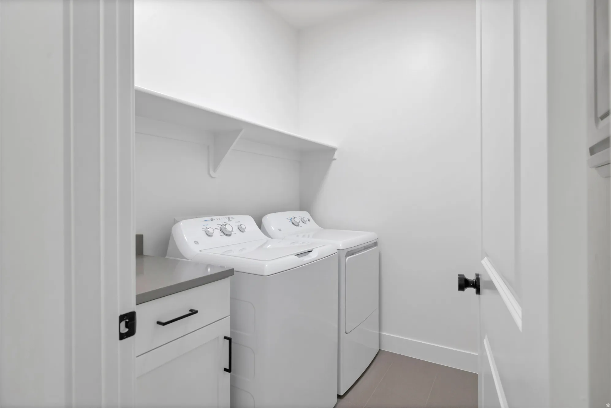 Laundry area featuring a built-in counter, integrated shelving, and white cabinetry with dark hardware