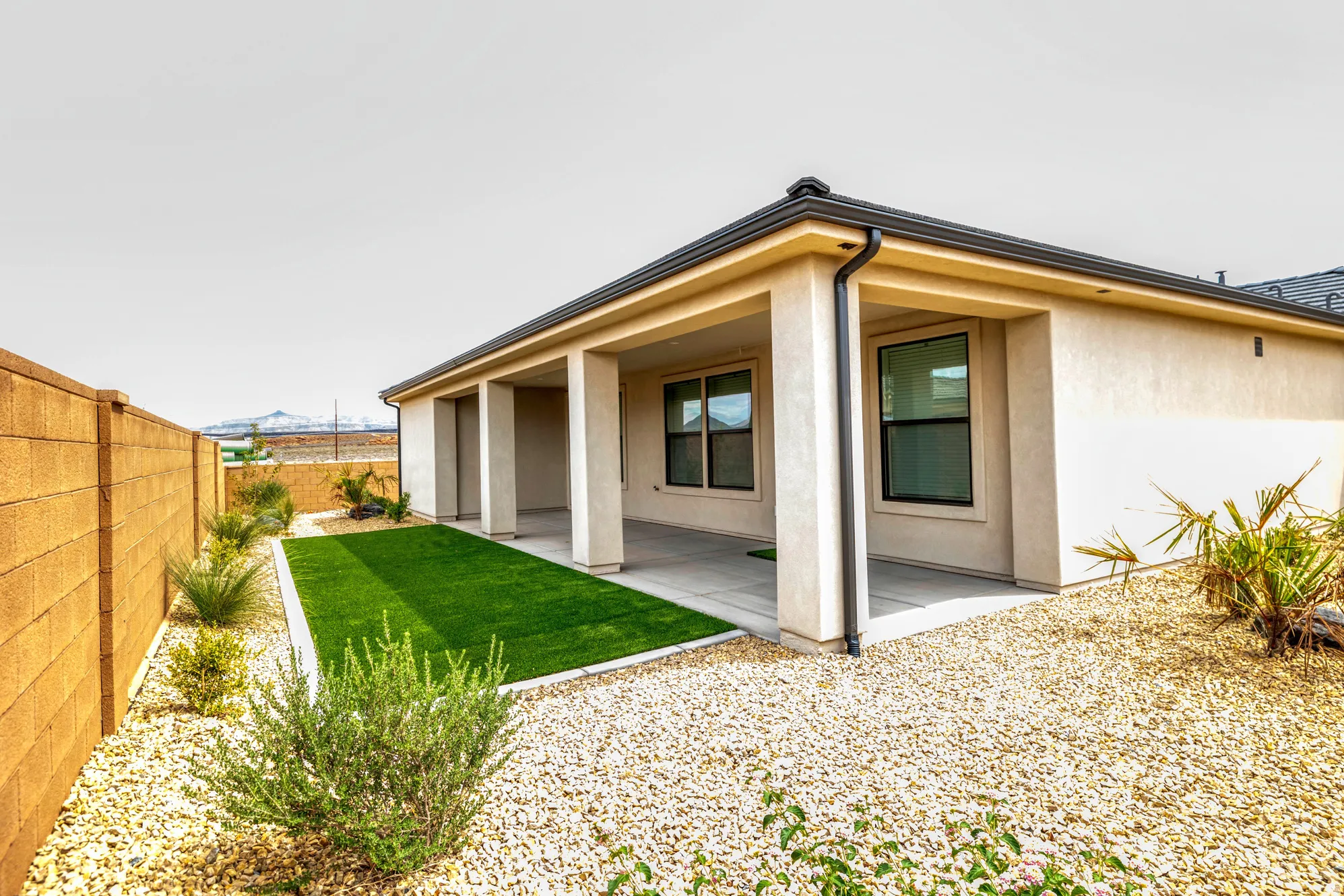 Covered patio with concrete flooring, artificial turf, decorative gravel, and stucco exterior