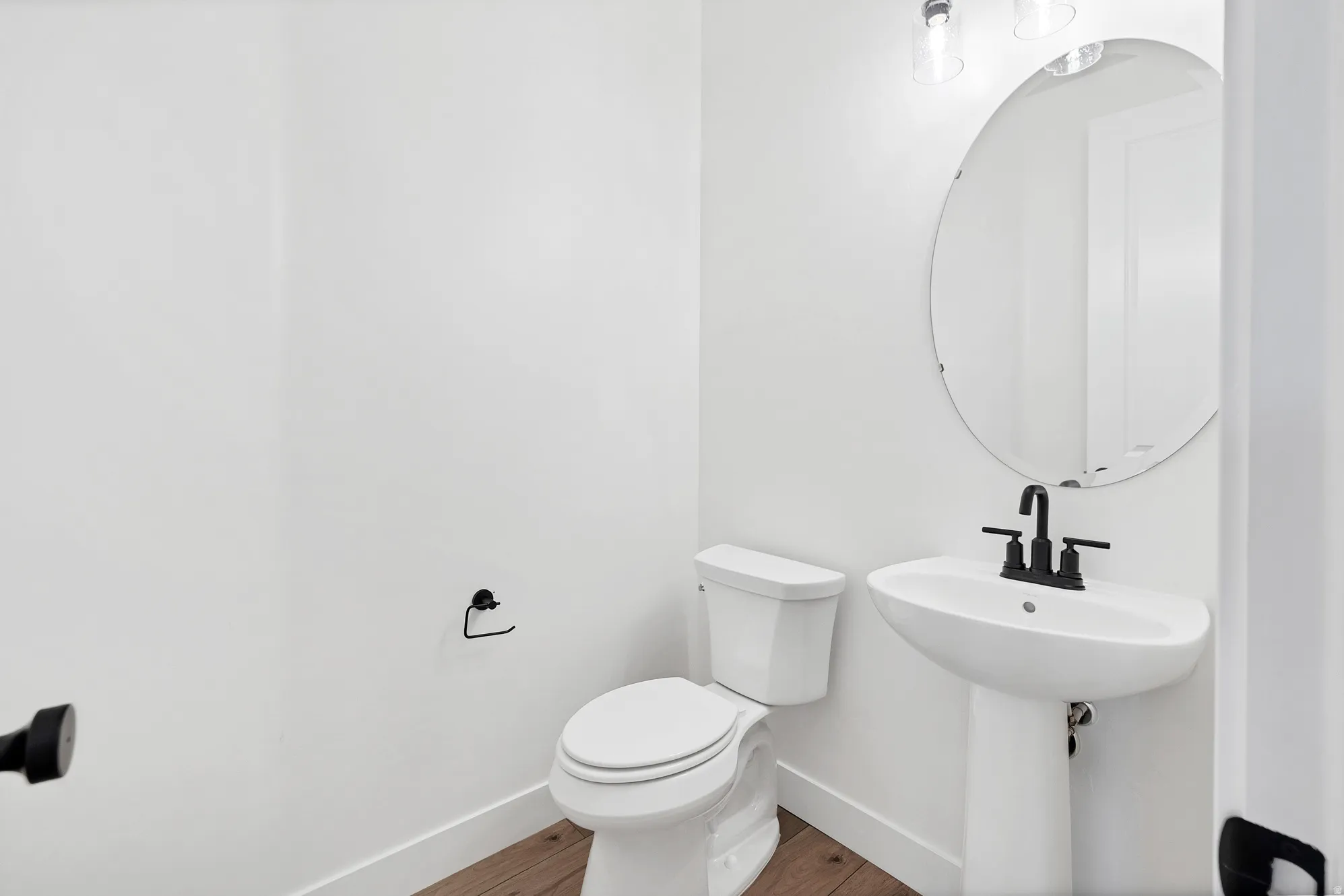 Pedestal sink with matte black faucet, oval mirror, and wall-mounted light fixture