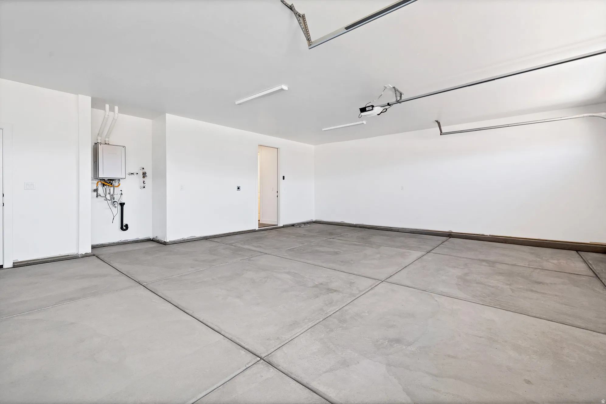 Spacious garage featuring a tankless water heater, smooth concrete flooring, and an automatic garage door opener