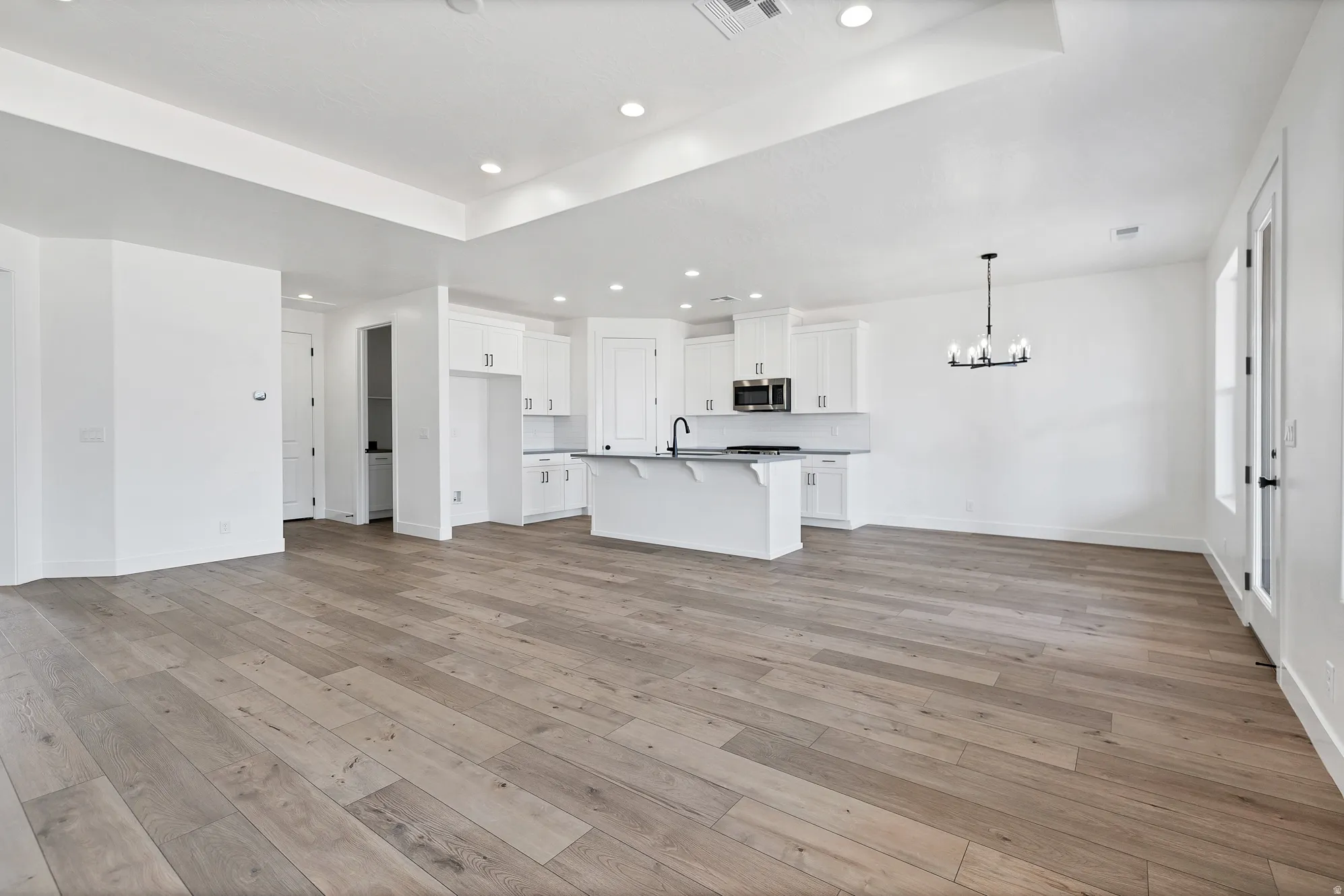 Open-concept living area featuring wood-finish flooring, recessed lighting, and a modern chandelier