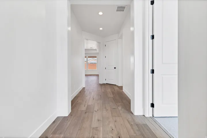 Hallway featuring wood-finish flooring, recessed lighting, white panel doors, and a bright interior