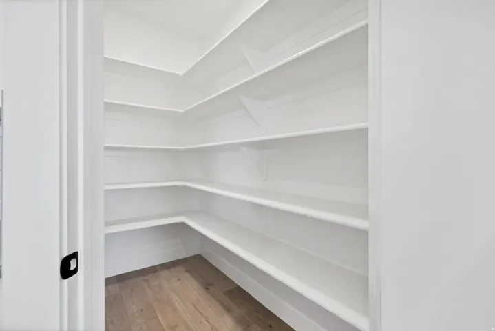 Walk-in pantry featuring extensive white shelving and wood-finish flooring
