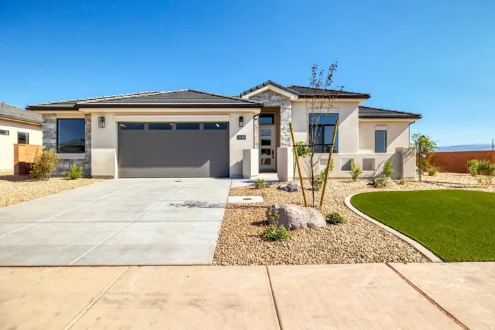 Contemporary stucco exterior with stone accents, an attached garage, and xeriscaped landscaping featuring artificial turf