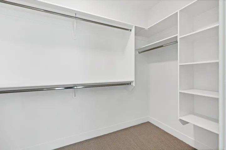 Built-in closet shelving, dual chrome hanging rods, recessed lighting, and carpeted flooring