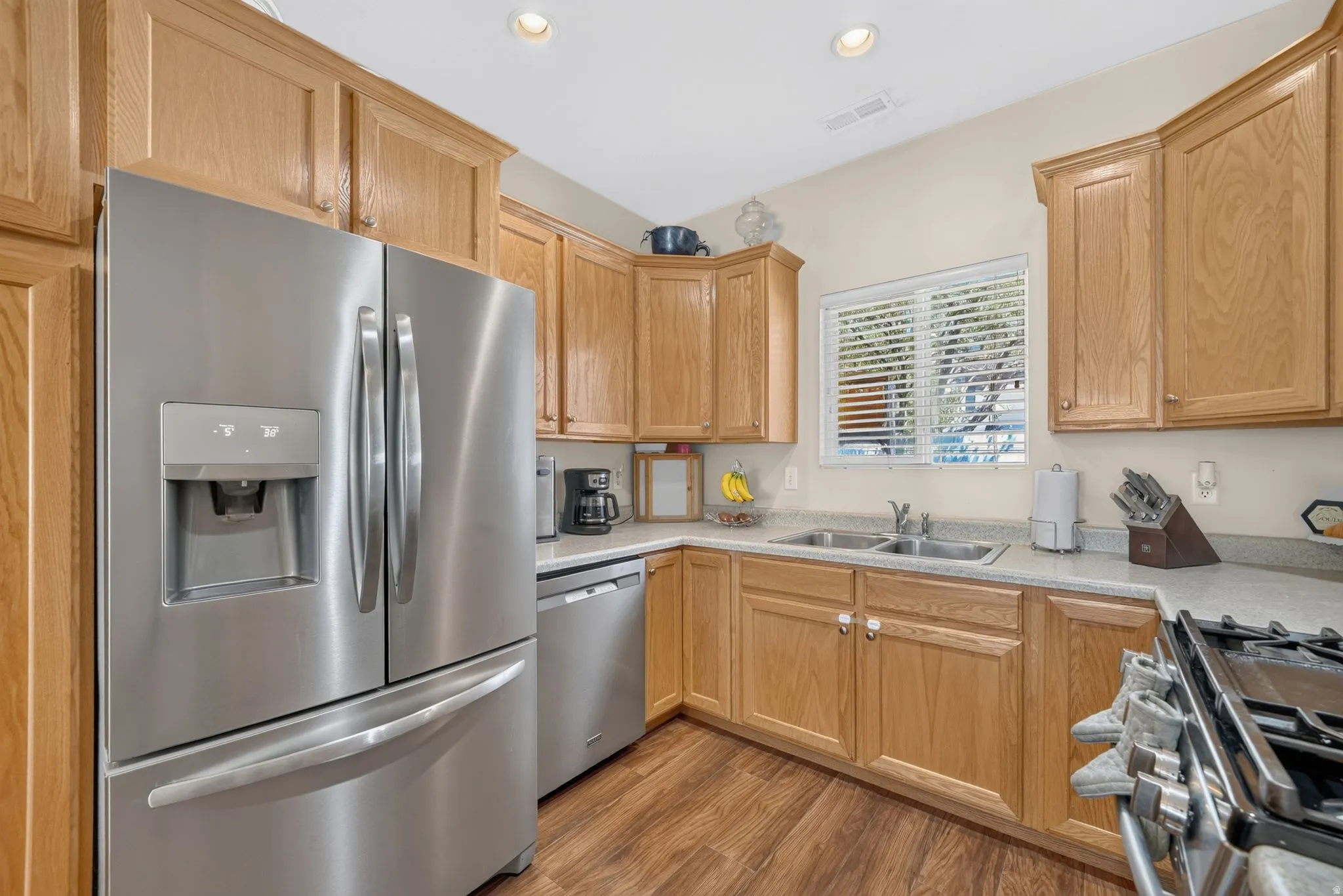 Stainless steel appliances, recessed ceiling lighting, wood-finish flooring, light-toned cabinetry, and a double basin sink