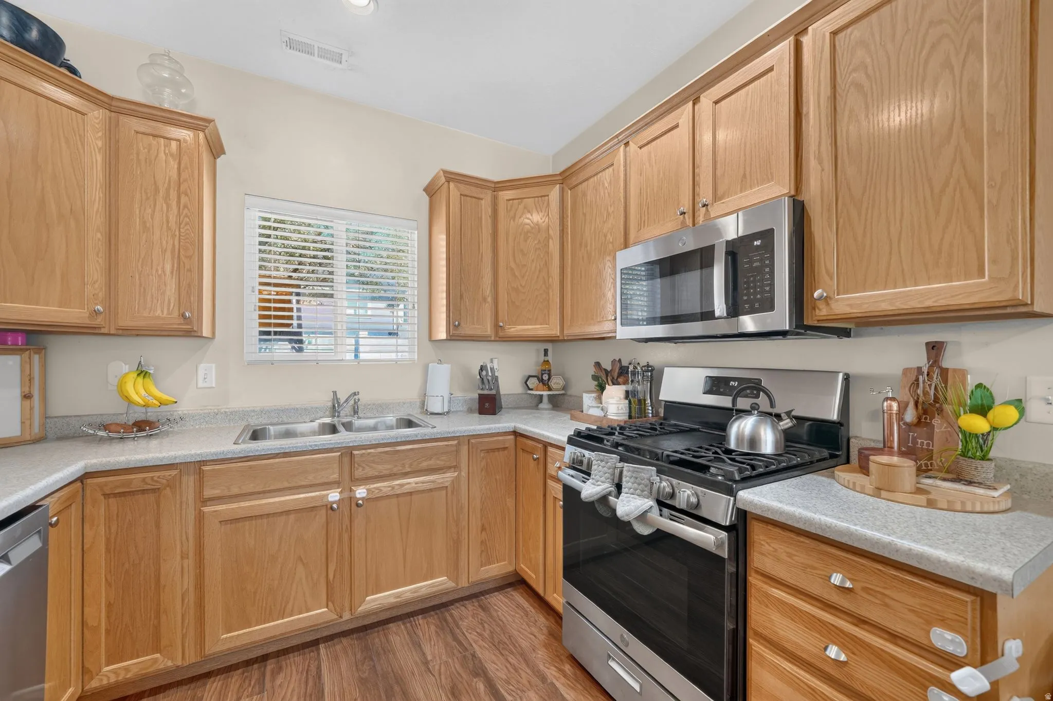 Wood-finish flooring, wood cabinetry, stainless steel appliances, double basin sink, and ample countertop space