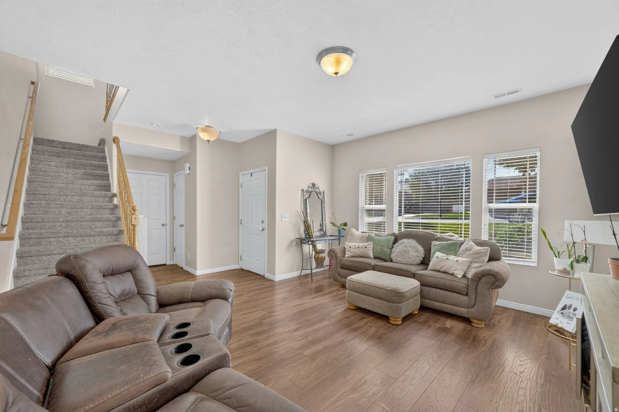Wood-finish flooring throughout, multiple windows with blinds, recessed lighting, and a carpeted staircase with wood handrails