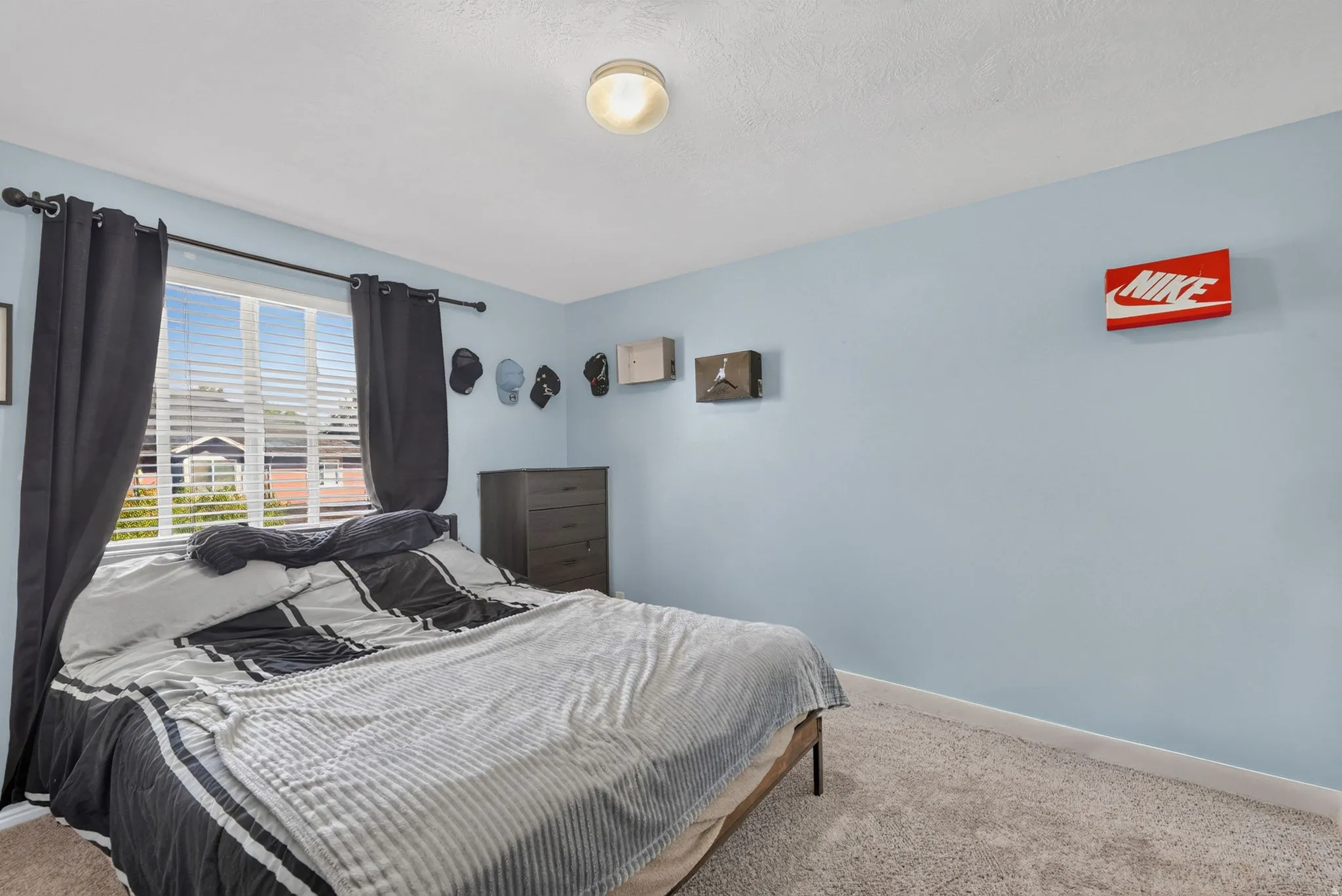 Carpeted flooring, window with blinds, ceiling-mounted light fixture, and a dresser