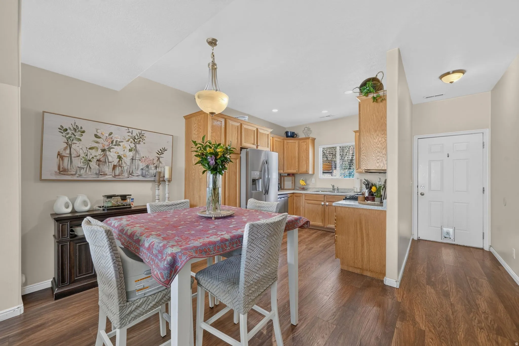 Wood-finish flooring throughout, with a kitchen featuring light wood cabinetry, stainless steel appliances, and a window above the sink