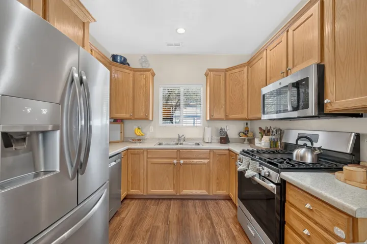 U-shaped kitchen with wood-finish flooring, light wood cabinetry, stainless steel appliances, and a window with blinds