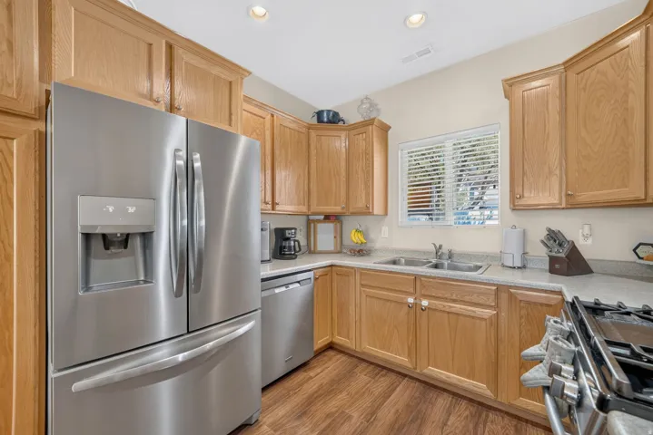 Stainless steel appliances, recessed ceiling lighting, wood-finish flooring, light-toned cabinetry, and a double basin sink