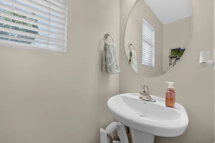 Pedestal sink with chrome faucet, oval wall mirror, and window with blinds