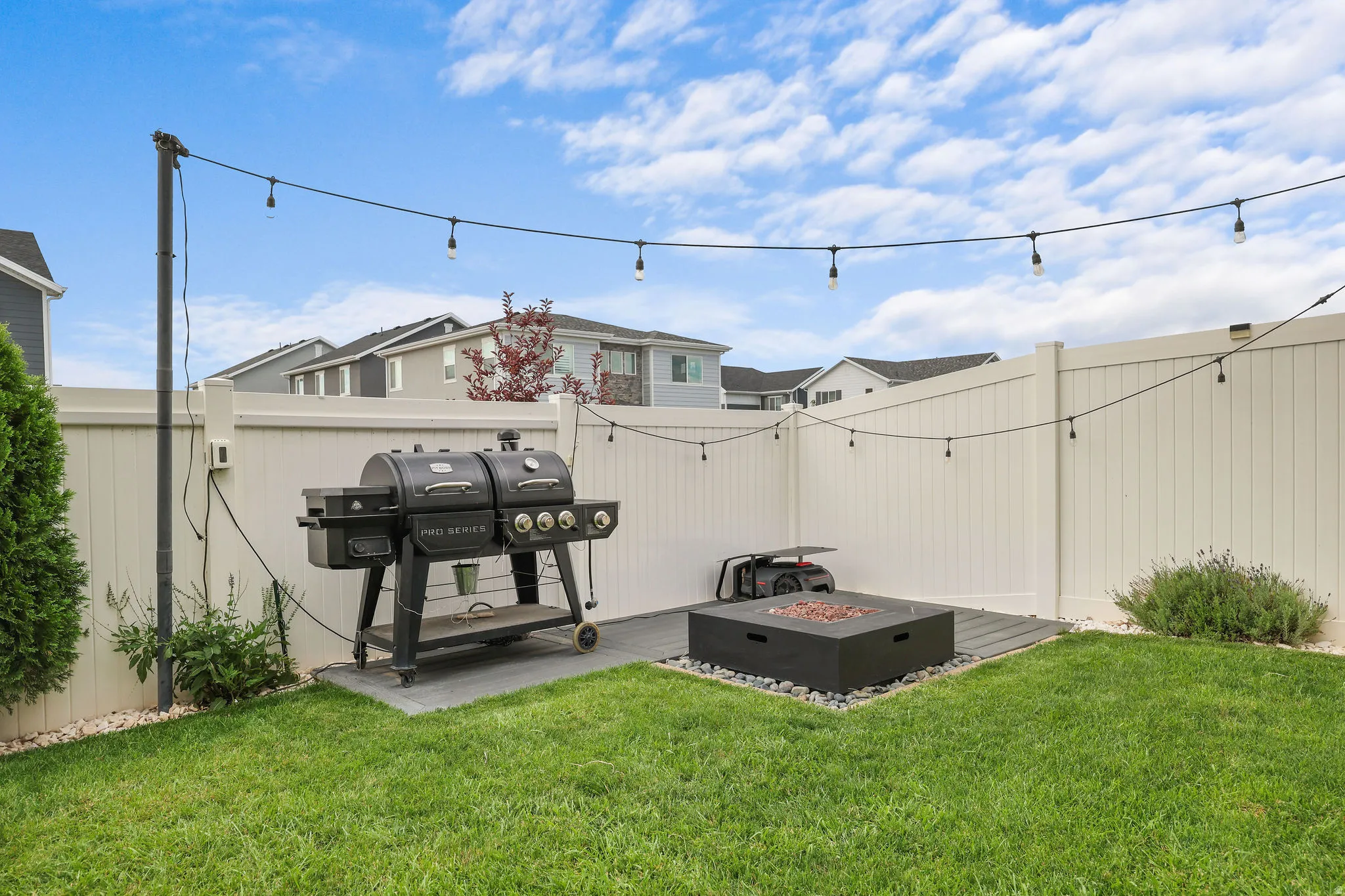 Manicured lawn, privacy fence, string lighting, and a fire pit with surrounding gravel