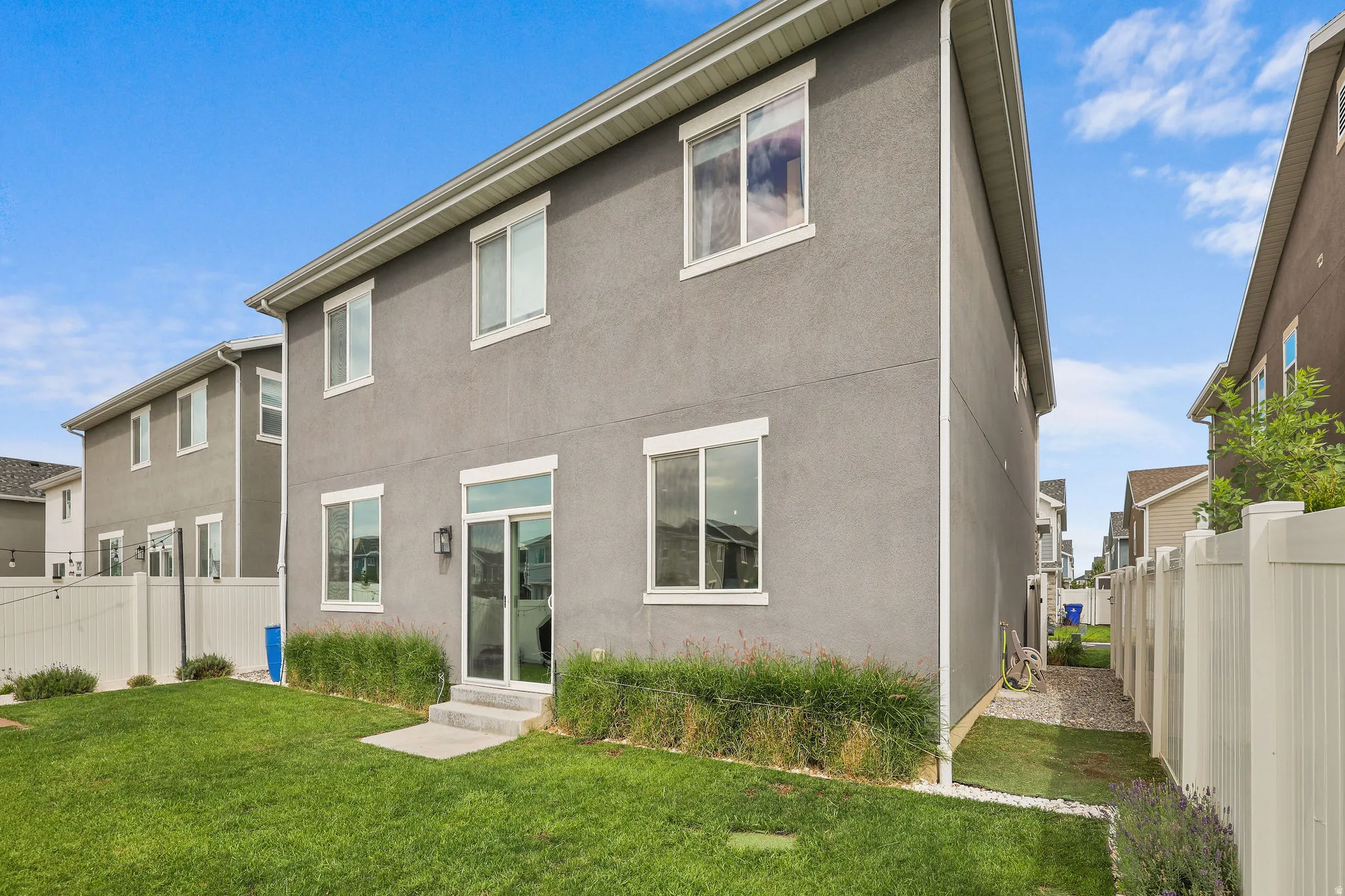 Gray stucco exterior, white trim windows, sliding glass door, concrete patio, and a manicured lawn