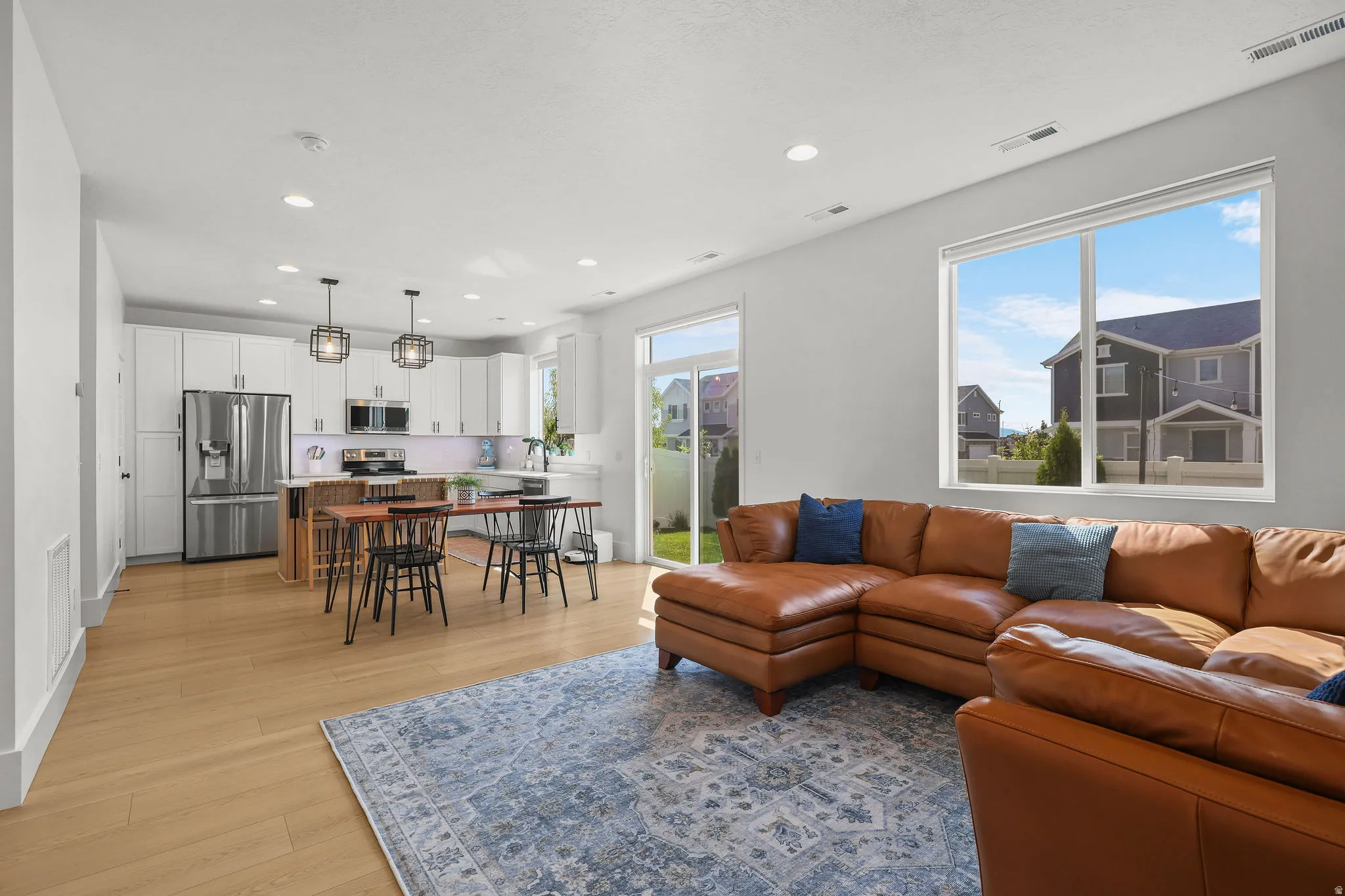 Open-concept living space featuring wood-finish flooring, white cabinetry, stainless steel appliances, and large windows