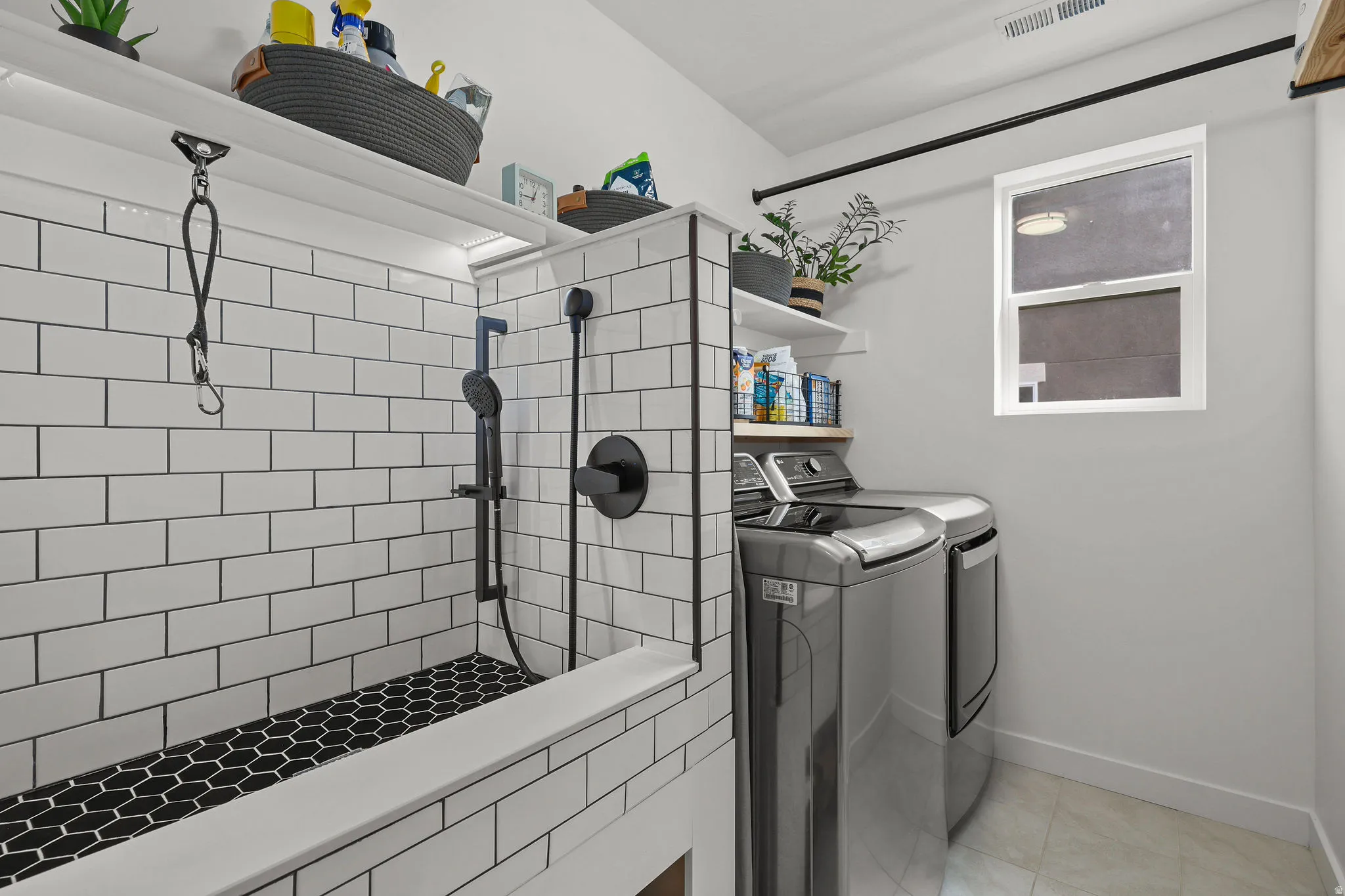 Integrated laundry area featuring tile flooring, a window, and a built-in wash station with subway tile surround, black hexagonal tile base, and matte black fixtures