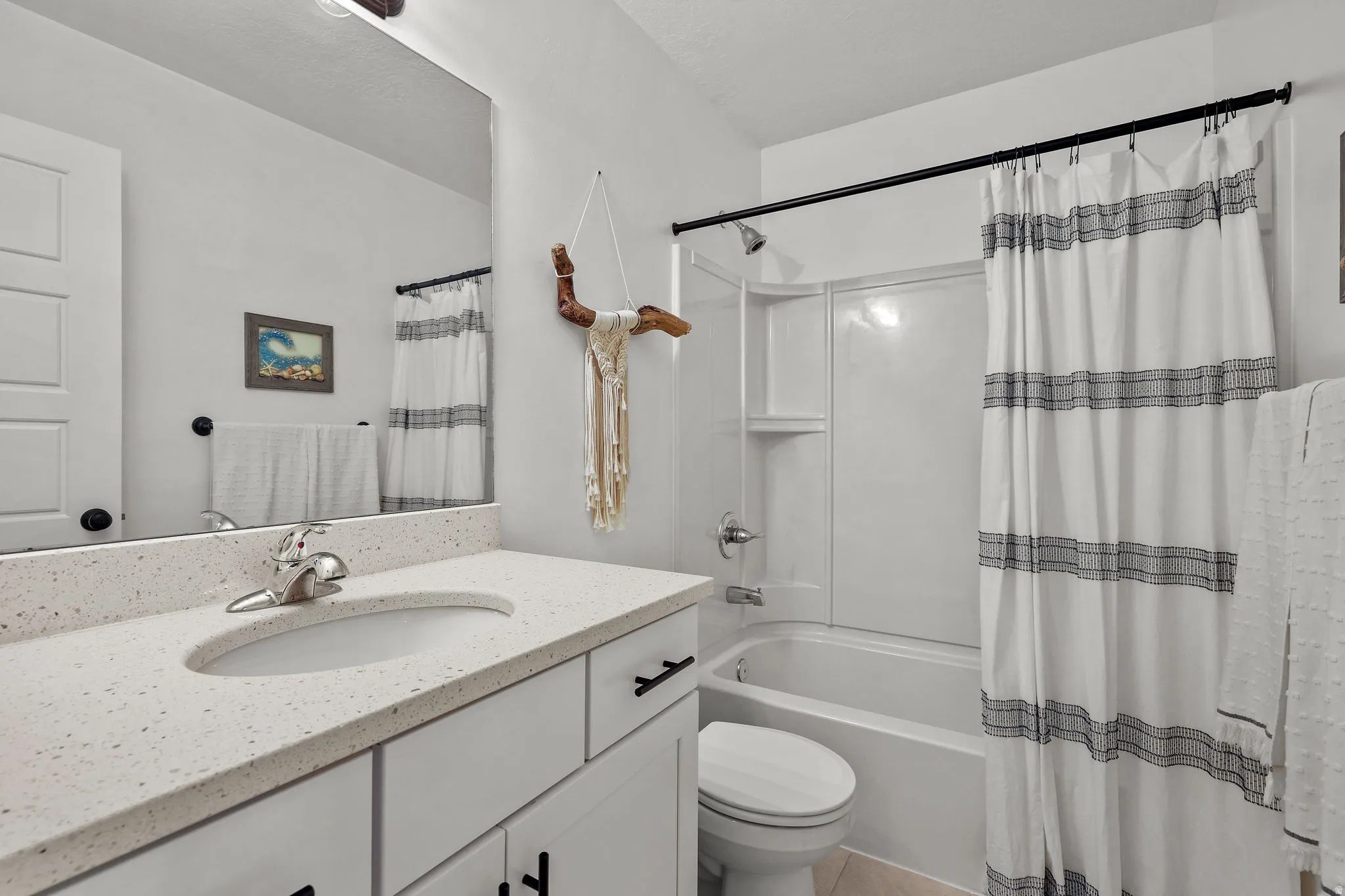 White shaker-style vanity with dark hardware, a single basin sink, and a speckled countertop