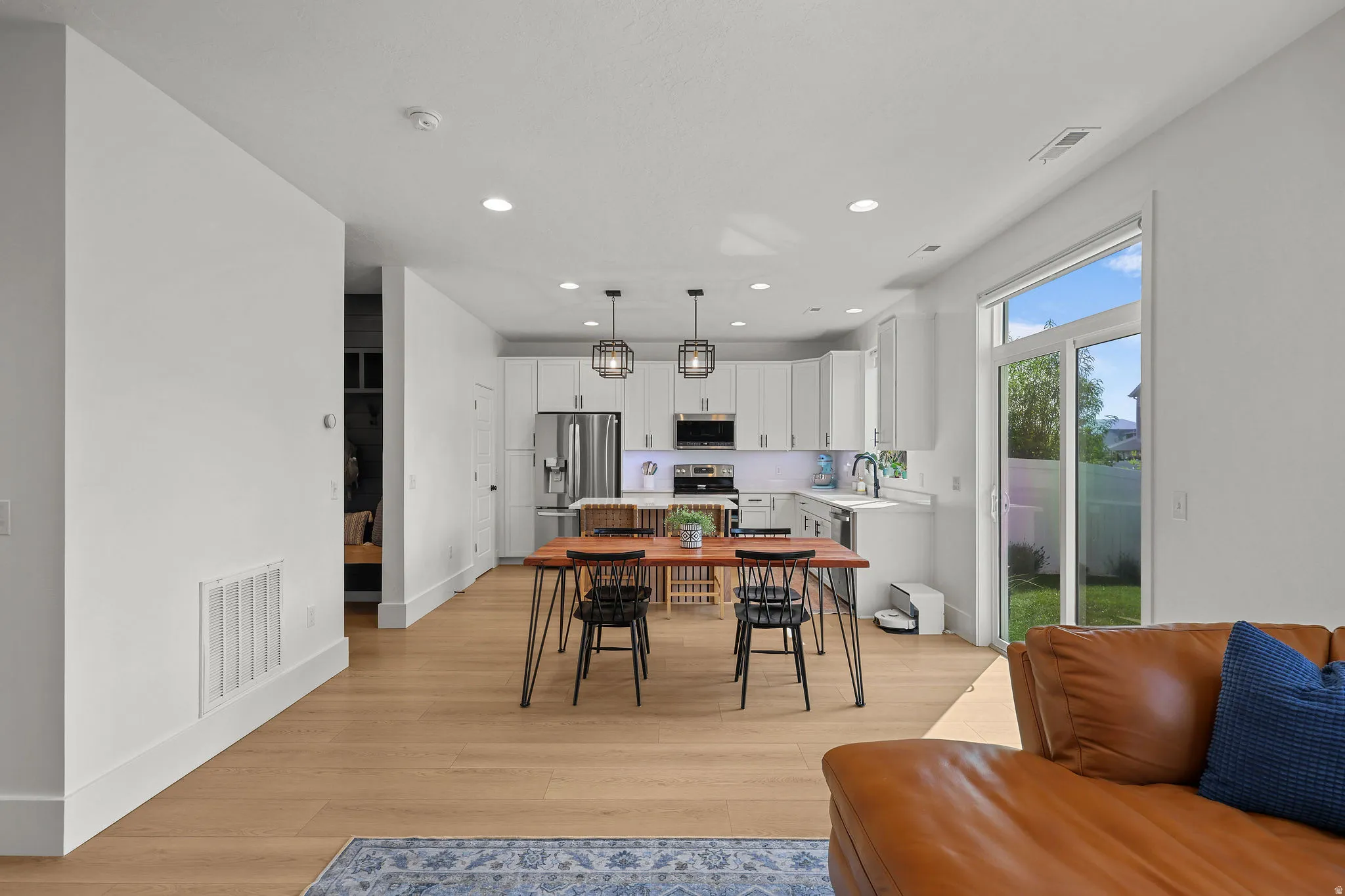 Open-concept living space with wood-finish flooring, white cabinetry, stainless steel appliances, and a sliding glass door to the backyard
