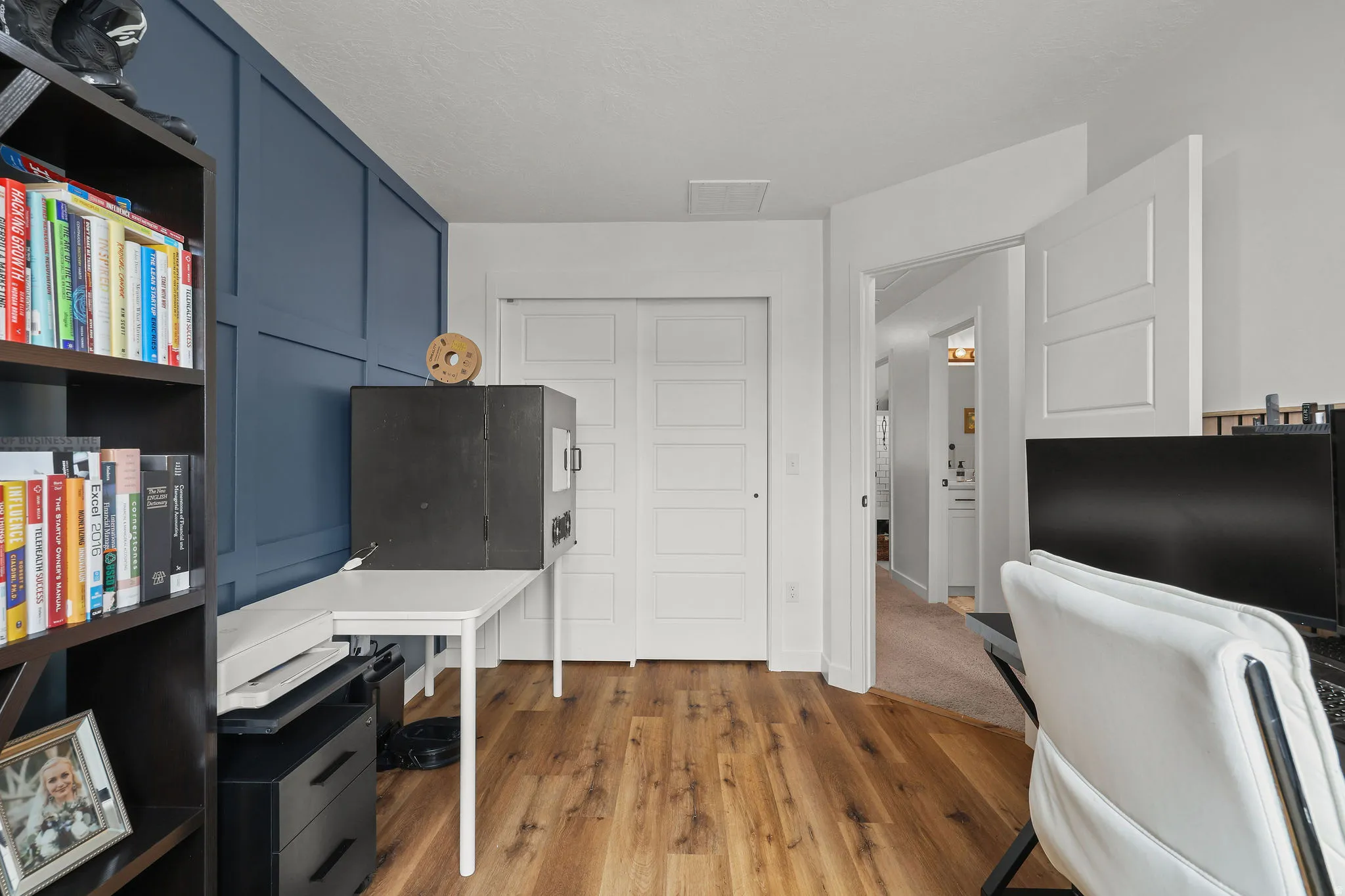 Wood-finish flooring, accent wall with panel molding, white paneled doors, and ceiling access panel