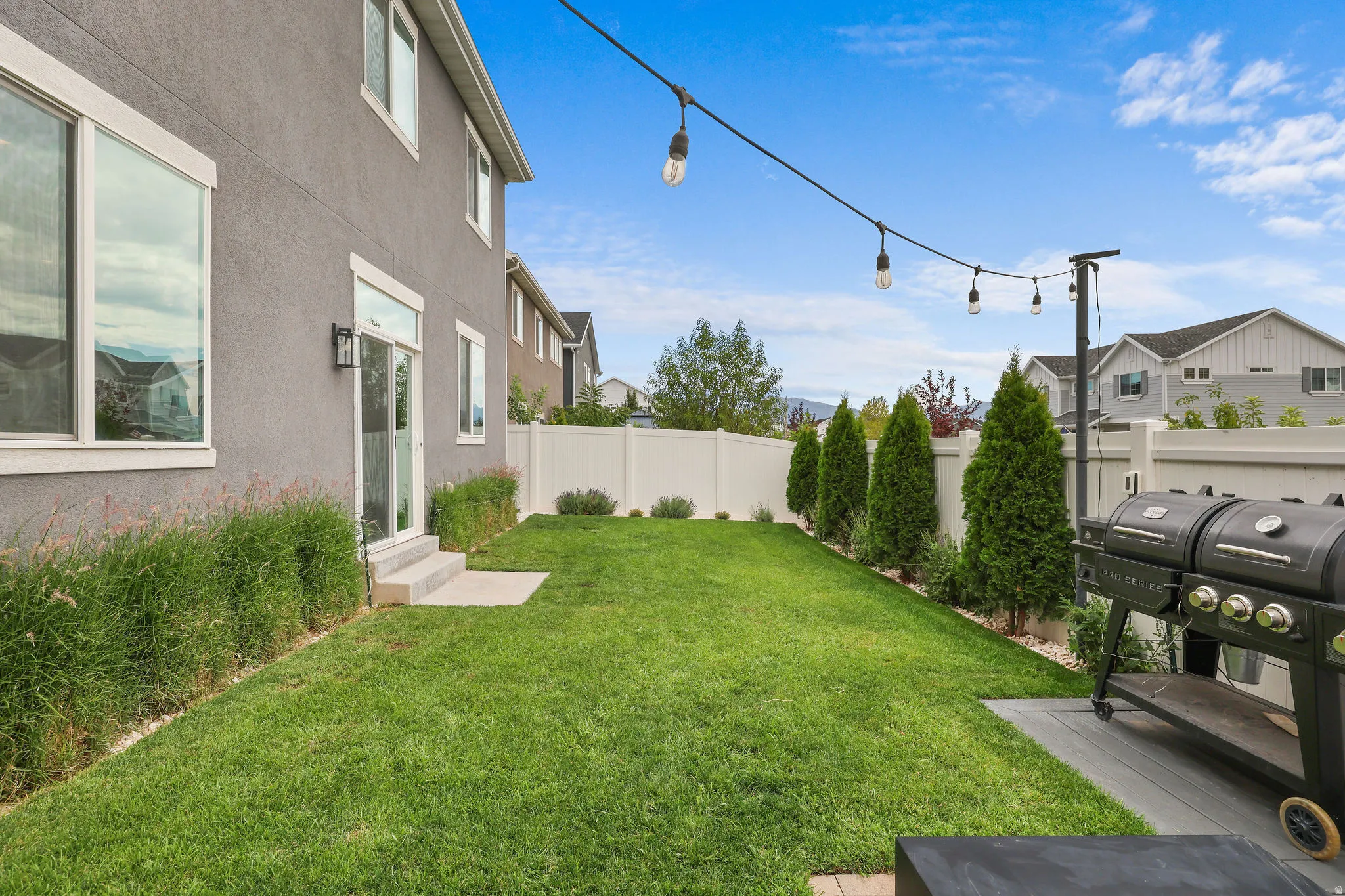 Rear exterior featuring a stucco facade, string lighting, a concrete patio, and a fenced yard with mature landscaping