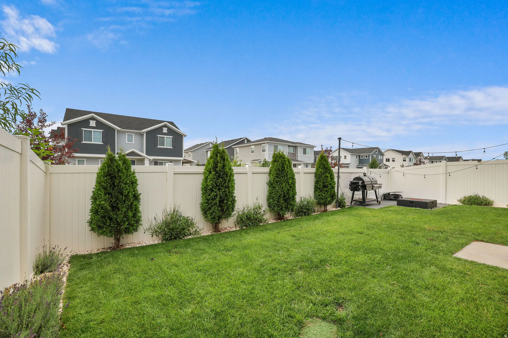 Expansive fenced backyard featuring a grassy lawn, decorative shrubs, and established trees