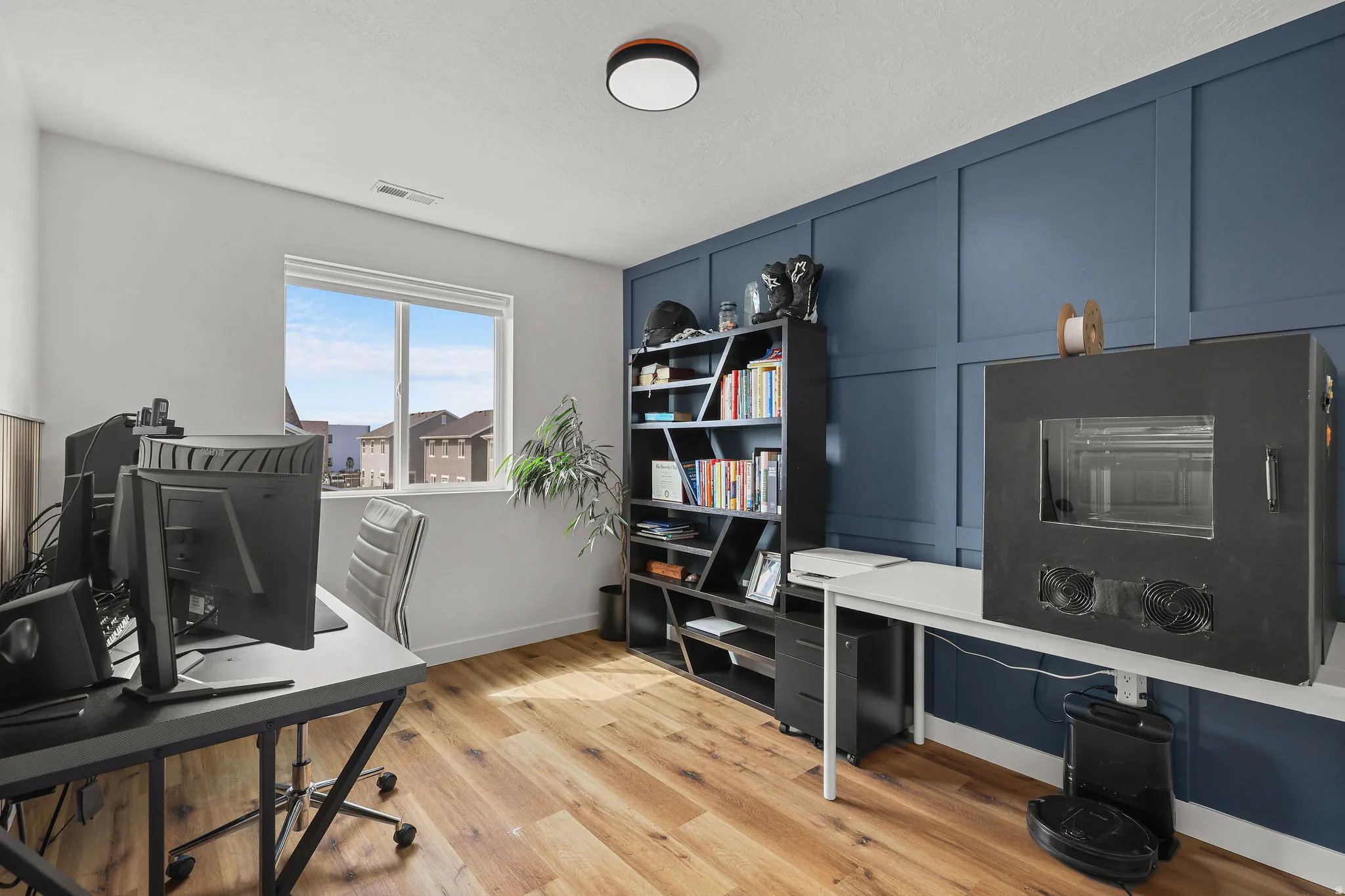 Wood-finish flooring, accent wall with paneling, built-in shelving, white window trim, and a flush-mount ceiling light