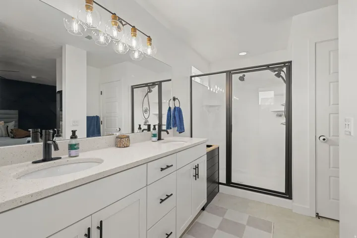 Dual vanity with integrated sinks and black matte faucets, white cabinetry with black hardware, and a glass-enclosed shower with a black frame