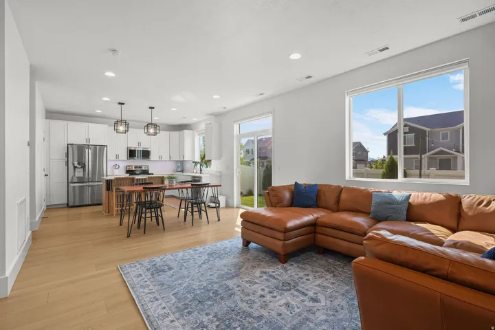 Open-concept living space featuring wood-finish flooring, white cabinetry, stainless steel appliances, and large windows
