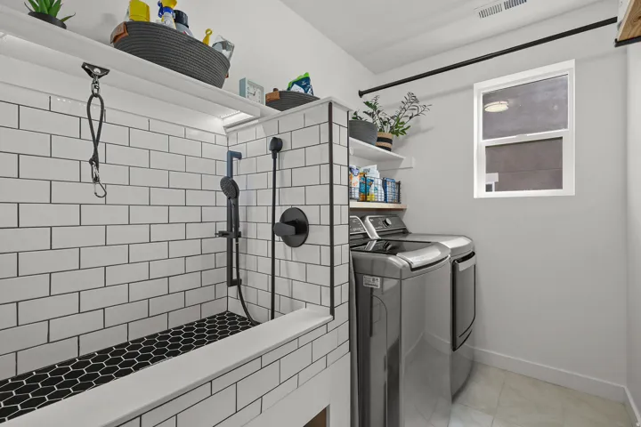 Integrated laundry area featuring tile flooring, a window, and a built-in wash station with subway tile surround, black hexagonal tile base, and matte black fixtures