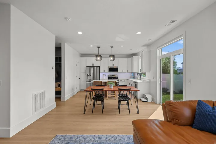 Open-concept living space with wood-finish flooring, white cabinetry, stainless steel appliances, and a sliding glass door to the backyard