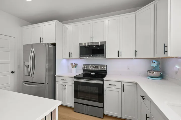 White shaker-style cabinetry with black hardware, stainless steel appliances, solid surface countertops, and wood-finish flooring