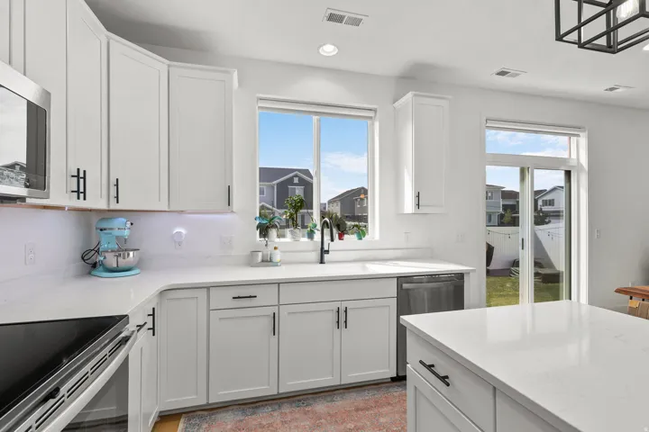 White shaker cabinetry with black hardware, white countertops, built-in dishwasher, integrated sink, and sliding glass door to outdoor space