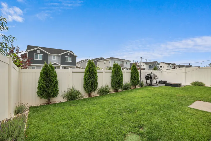 Expansive fenced backyard featuring a grassy lawn, decorative shrubs, and established trees