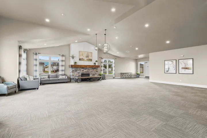 Vaulted ceilings with recessed lighting, stone-clad fireplace with wood mantel, large windows, and patterned carpet flooring