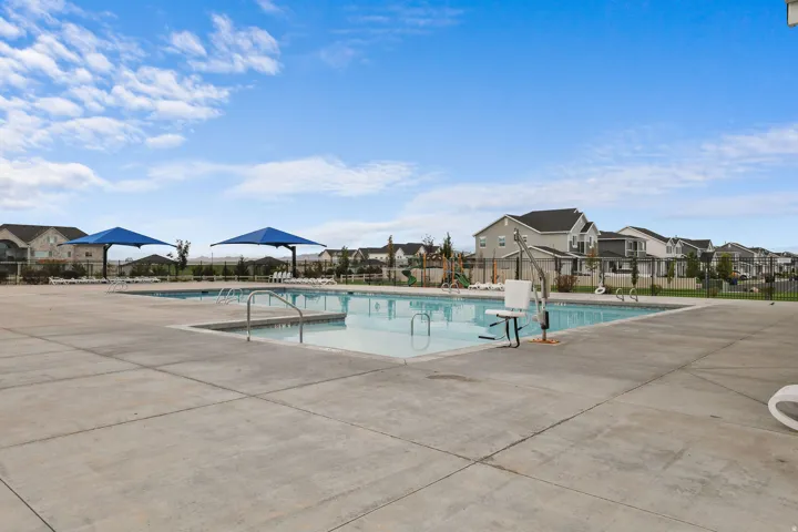 Expansive concrete pool deck featuring two swimming pools, permanent shade structures, and surrounding residential properties